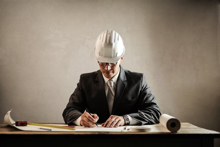 Services Engineer in a suit drafting architectural plans at a desk indoors.